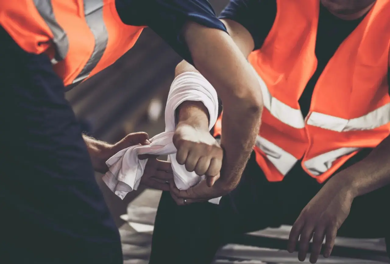 People in orange safety vests applying cloth/packing to a wound on a person.