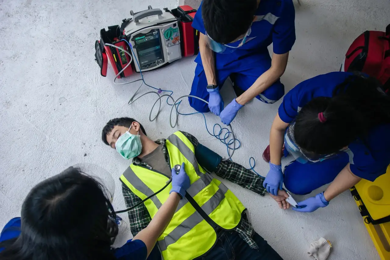 Rescuer in blue gloves attaching AED electrode wires to a person lying on the ground.