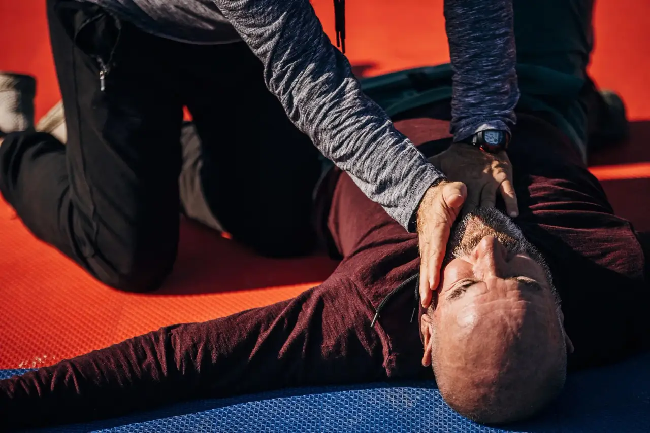 Person lying on their side while another places a hand near their head (recovery position).