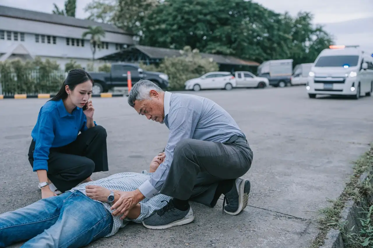 Man kneeling beside a person lying down outdoors, checking on them.